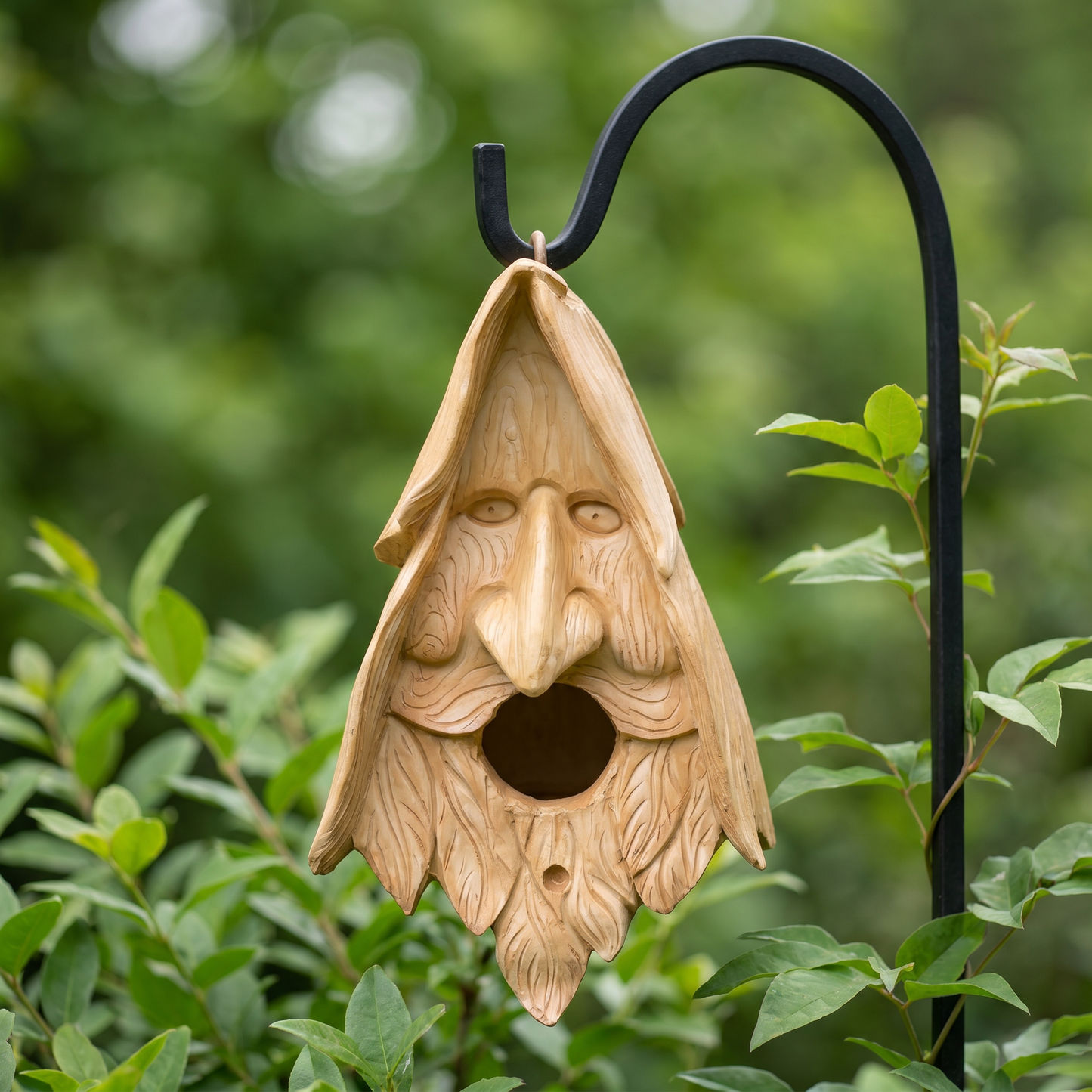 Wood spirit birdhouse hanging from a wrought-iron garden hook among green foliage