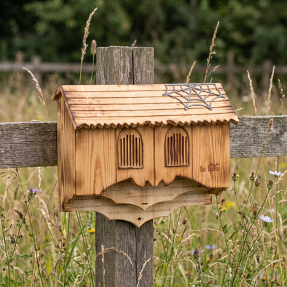 Carved gothic bat house on a garden fence post in a wildflower meadow