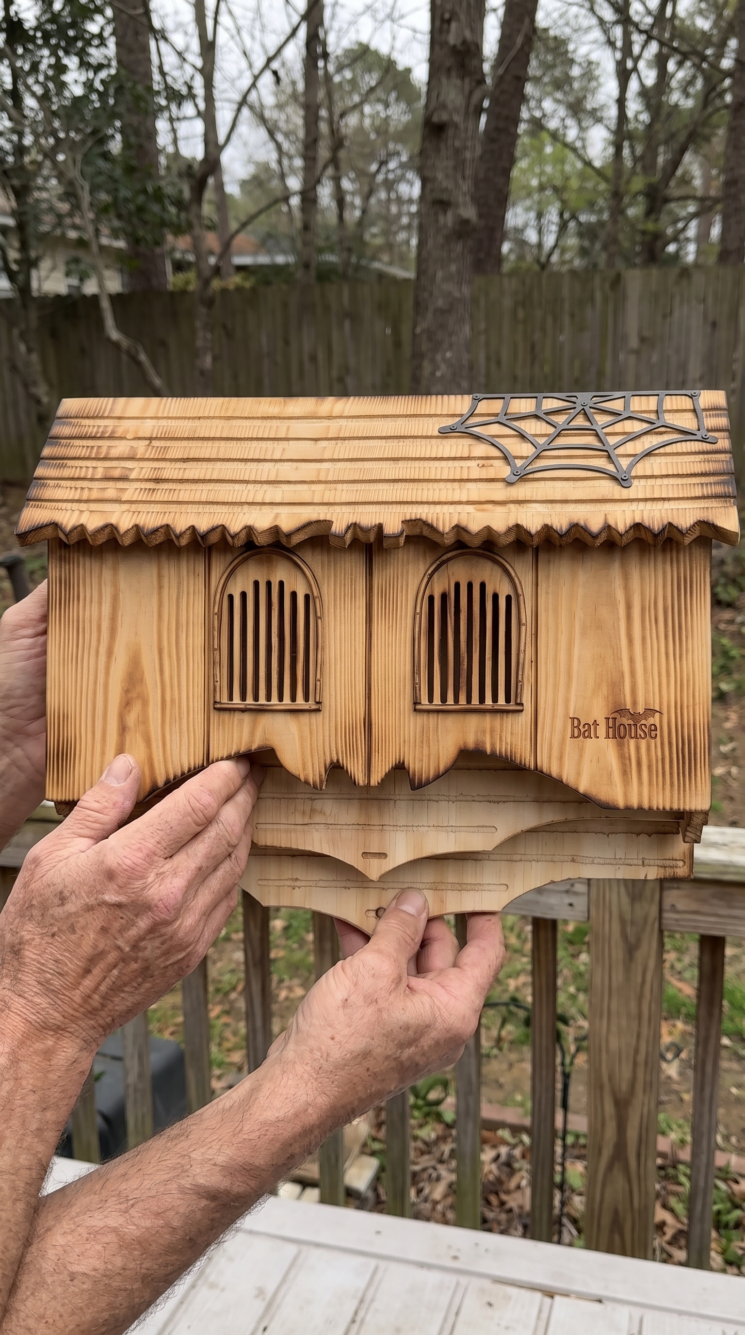Weathered hands holding the carved gothic bat house